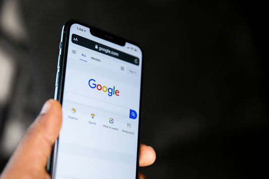 A hand holding a smartphone displaying the Google search engine homepage